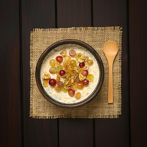 纤维坚果甜的燕麦粥加葡萄和核桃在生锈碗中的胡桃侧面有木勺子用自然光照黑木头图片