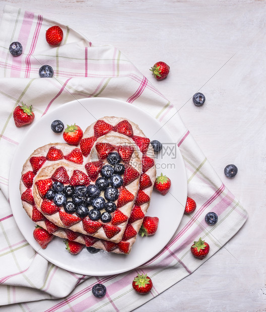 乡村浆果夏天鲜新美味的自制蛋糕配有草莓和蓝以心为形式粉红白餐巾纸在生皮木本底图片