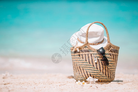 白色海滩上的编织包和墨镜遮阳帽图片