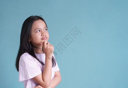 亚洲小女孩站着思考把手放在下巴她的蓝色背景与世隔绝女学生在家工作知识图片