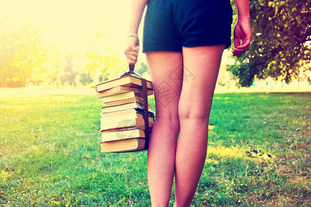一个女孩提着一堆书走在绿色草地上图片