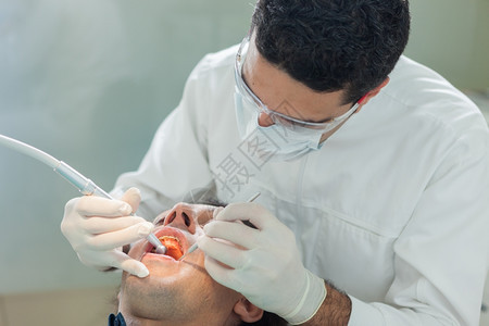 健康诊所成人男牙医对40岁病人进行卫生治疗的照片男牙医为一名40岁的病人提供卫生治疗的相片图片