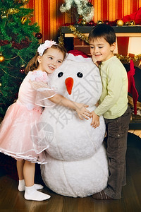 假期两个美丽的孩子和玩具雪人在圣诞树附近前夕新的图片