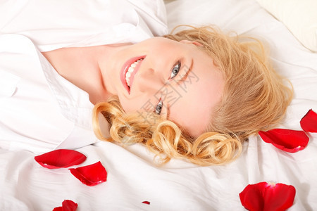 带着红玫瑰花瓣躺在床上的金发快乐女人红色的明亮图片