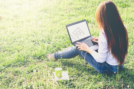 白色的商业成人女孩用笔记本电脑在绿色的田地里阳光清晨装模作样古老的音调图片