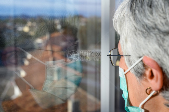 戴防护面罩的高级妇女在家透过窗户看冠状检疫的概念待在家里和社会疏远锁定老年人和退休的生活方式戴防护面罩的高级妇女在家透过窗户看冠图片