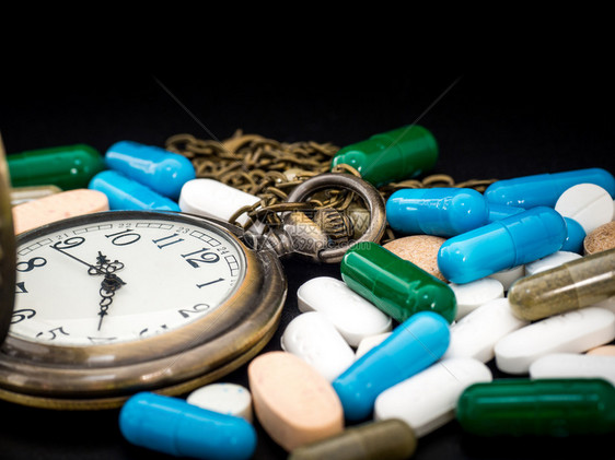 多色和胶囊的古董时钟在黑底背景上我们反对抗用容器治愈健康绿色蓝白圆形胶囊药丸的治疗器处方药品抗生素图片
