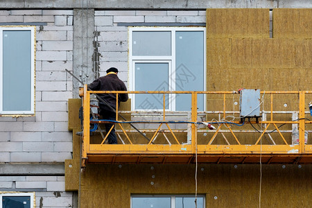 外部的安装男建造者使用筑摇篮矿棉将房屋的正面绝缘建造者用矿物绝缘材料将房屋的正面绝缘图片