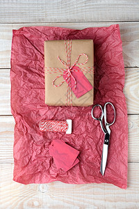 生日角度展示红色和白绳子绑在一块红纸上的礼物面有剪刀绳子卷和白木桌上的礼品标签赠放在一张红纸上面贴有剪刀绳子和礼品标签图片