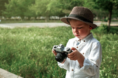 保持一种白小男孩在公园里穿着旧衣服手拿一个旧提箱和台反光相机快乐的图片
