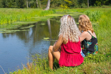 衣服姐妹友谊金发和红头的女人坐在水边一起图片