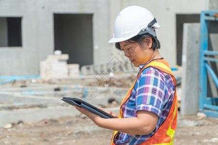 在建筑工地上站着时用平板头戴盔的亚洲女建筑工肖像以背景概念为构筑工程想在职的环境保持图片