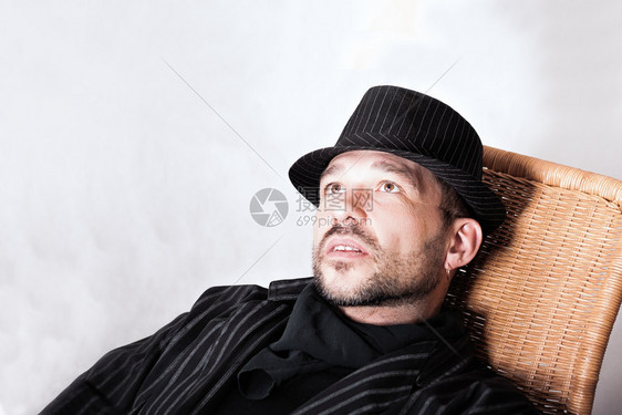 长着胡子的英俊男肖像他戴着黑帽子耳穿坐在椅子上用皮尔斯德耳朵戴黑帽子的领结男气概时尚图片