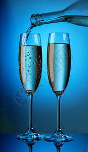 庆祝诱人的瓶子里芳香槟倒入蓝色背景的两个玻璃杯中瓶子里的芳香槟倒入两个玻璃杯中浪漫的图片