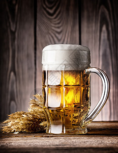 马克杯棕色的小麦木质背景上带泡沫和耳朵的多面淡啤酒杯带泡沫和耳朵的多面淡啤酒杯图片