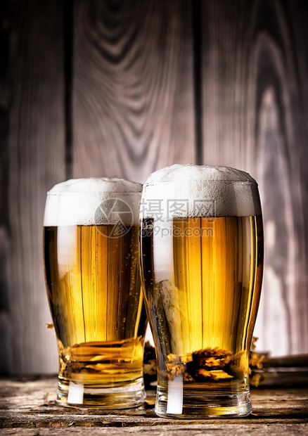 两杯木质背景上带泡沫的淡啤酒两杯带泡沫的淡啤酒食物桶图片