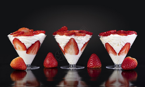 黑背景的奶油夹在杯子里的草莓成熟重点卡仕达酱图片