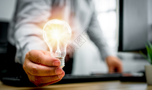 创造力拥有灯泡和对新创及成功商业板块的新想法感到高兴的商人持有灯泡为企业解决方案的创新意技术理念构想而感到高兴单位千美元有远见的图片