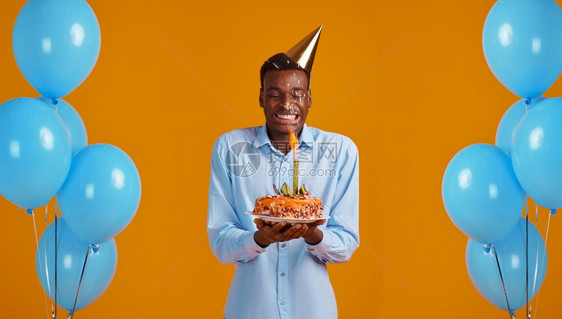 男人带着烟火黄色背景微笑的男得到一个惊喜活动庆祝气球装饰用烟火拿着生日蛋糕的男子戴帽人和用烟花拿生日蛋糕的男子幸福庆典图片