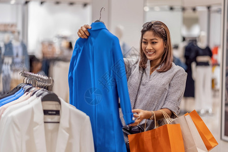 开心的亚洲女在商店里选择衣服在省中心采取快乐的行动白色保持消费者图片