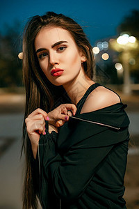 优雅的华丽女穿着黑色晚礼服在城里摆着摄影机的美丽年轻模特女郎图片
