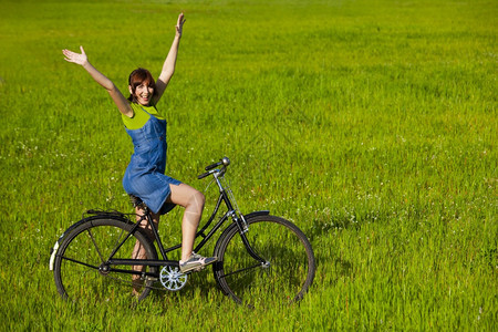 休闲的年轻骑自行车快乐年轻姑娘在绿色草地上骑着一辆旧自行车图片
