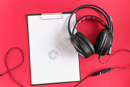 多于最佳黑色耳机和剪贴板记事本红色背景上带有白空纸概念收听音频材料和摘要远程教育顶视图复制空间的图片