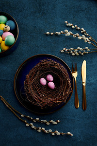 棕柳树枝筑巢中的东鸡蛋和蓝布背景的桌餐具春树开花和烧菜庆祝节日的新花卉装饰活动标志柳树枝蜂巢中的东鸡蛋和餐具分支花的图片