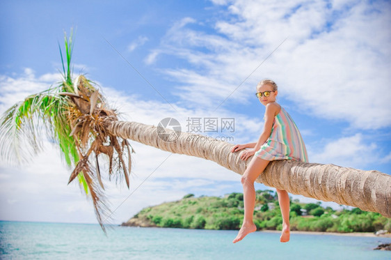 热带海滩上可爱的小女孩坐在棕榈树上图片