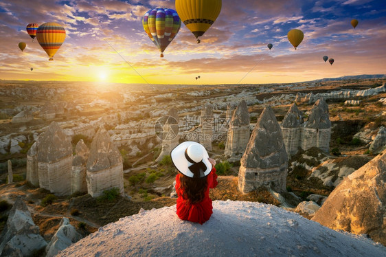 空气热的夏天在土耳其卡帕多西亚的日出时坐着看热气球的妇女图片
