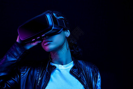 技术肖像身着眼镜的非裔美国年轻女子观看360度视频其虚拟现实头盔在亮光中的黑色背景上被隔离注数字的图片