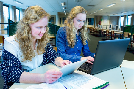 集中自习在线的两个长头发天主教姐妹在计算机室电脑和平板上工作妇女图片