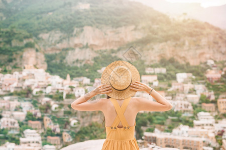 年轻的意大利阿马尔菲海岸的意大利村庄背景中戴草帽的年轻女子背影快乐后退图片