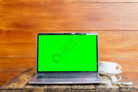 小样用空屏幕和咖啡杯智能手机在树枝桌边的咖啡厅店背景绿色屏幕上用空抽装笔记本电脑工作区数字的图片