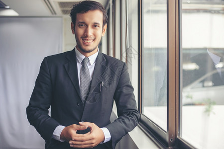 快乐的英俊商人站着微笑在办公室里工作商业年轻的图片