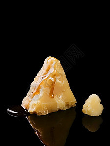 荷兰帕尔马干酪烤的一块片子关闭蜂蜜流动在奶酪上选择焦点奶酪被反射在一张黑桌子上意大利语图片