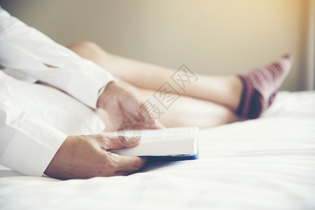 尽管喜欢看书的女读者坐在床上享受舒适放松的休闲时光概念白色舒适的床和年轻漂亮女孩读书教育和学习的概念纸谁图片