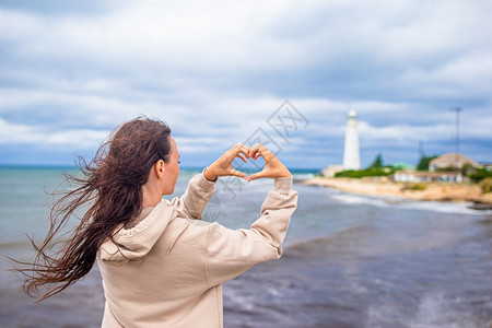 走丈夫靠近风暴海岸的旅游女客望着灯塔妇女步行到并创造心脏制作图片