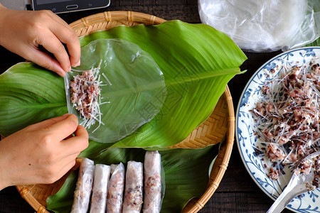 叶子妇女在家里做春卷或香焦自制食物用肉填料米纸包装在绿叶背景上手滚越南鸡蛋卷春天最佳图片
