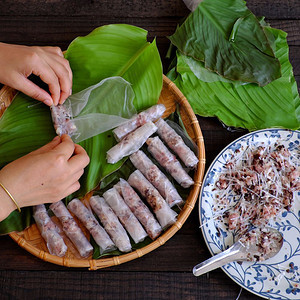 叶子材料春天妇女在家里做春卷或香焦自制食物用肉填料米纸包装在绿叶背景上手滚越南鸡蛋卷图片