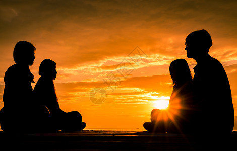 身体闲暇四位年轻人在海滩日出时坐木制码头上用橙色美丽的天空和云彩进行冥想日落图片