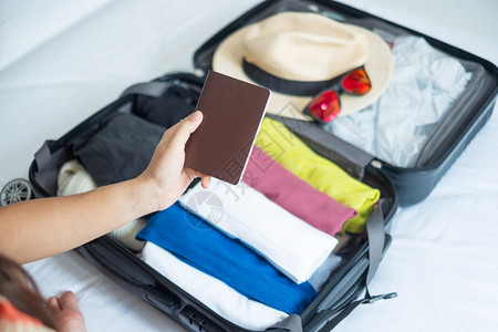 游客年轻成女为暑假旅游者打包行李旅检查名单随身李在床铺的手提箱内旅行附件时间放松旅行和周末概念休息年轻的图片