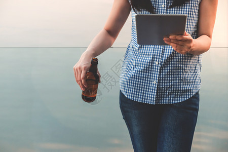 现代的人生活方式概念年轻女在夏季通过平板电脑阅读数据和喝啤酒站在河边的甲板上放松女士户外图片
