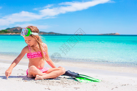 小女孩在沙滩上带着脚鞋和护目镜玩耍图片