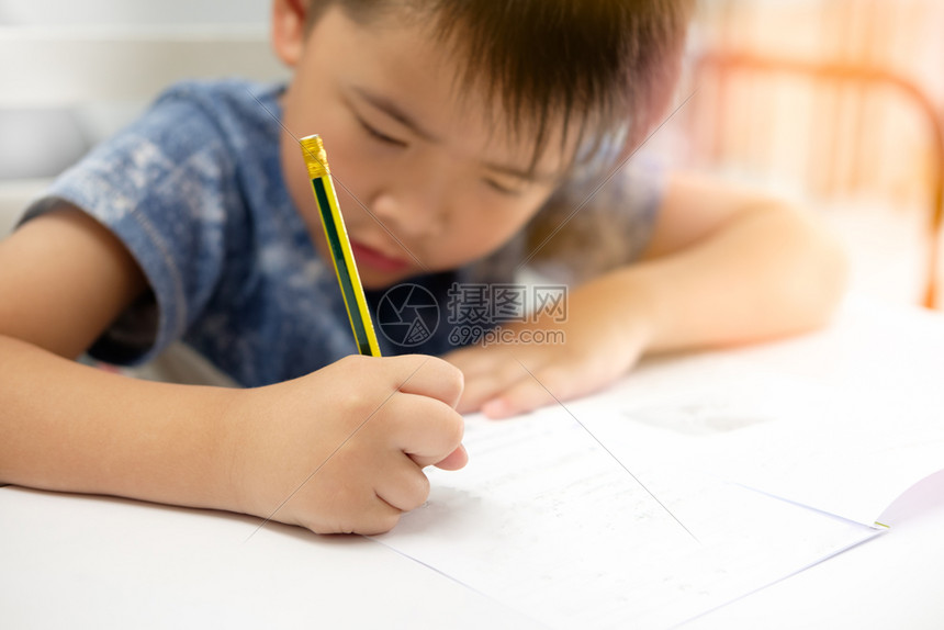 亚洲男孩正在做家庭作业和写与预期的脸装饰橙色灯光关注儿童铅笔书学校图片