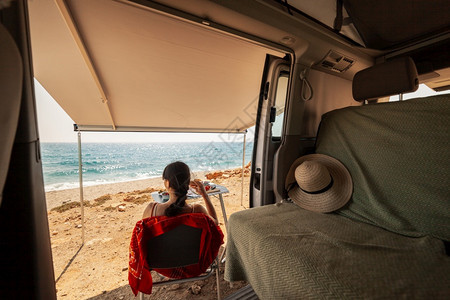年轻女子在她的大篷车里吃早餐看海滩美景图片