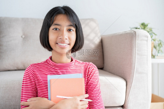 幸福快乐的亚洲女孩坐在客厅的地板上早和阳光下脸笑着亚洲儿童的肖像拿着书和快乐表达自信的概念在家学习生室内的图片