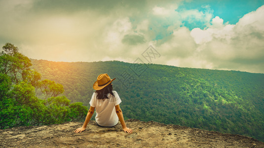 树木热带常绿身戴帽子坐在山顶悬崖的年轻旅行女青心情放松观看美丽的森林景色蓝天空和云彩风景在度假亚洲妇女独自旅行时图片