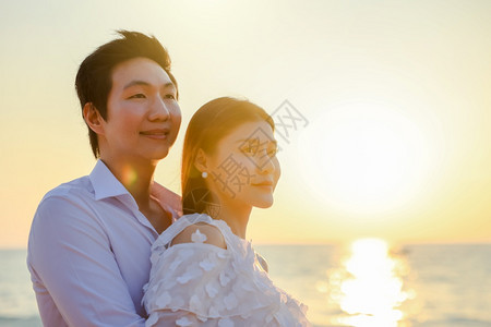 人们年轻快乐的亚裔夫妇在海滩上拥抱浪漫旅行蜜月渡假暑亚洲女和男在日落背景下手抱着户外步行海滨图片