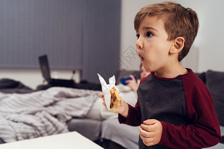 童年站在餐巾纸或糕饼中吃晚饭三明治的幼小儿童在夜边观食时张开的嘴前拿着餐巾纸或糕饼常设站立图片